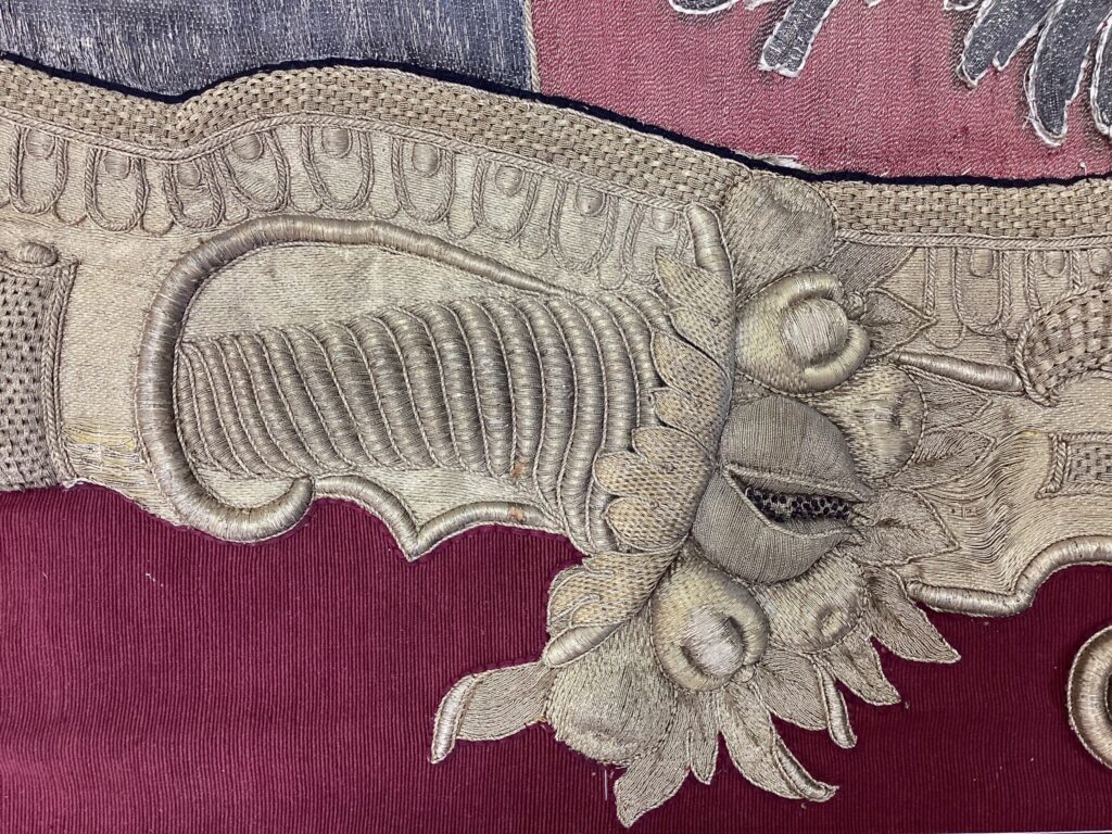 Detail der Goldreliefstickerei auf rotem Grund der Wappendecke