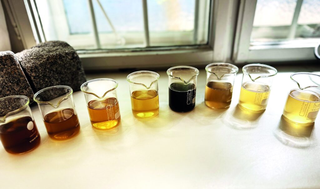 Glasbecher mit unterschiedlich gefärbten Wasserproben aus der Aerosolreinigung